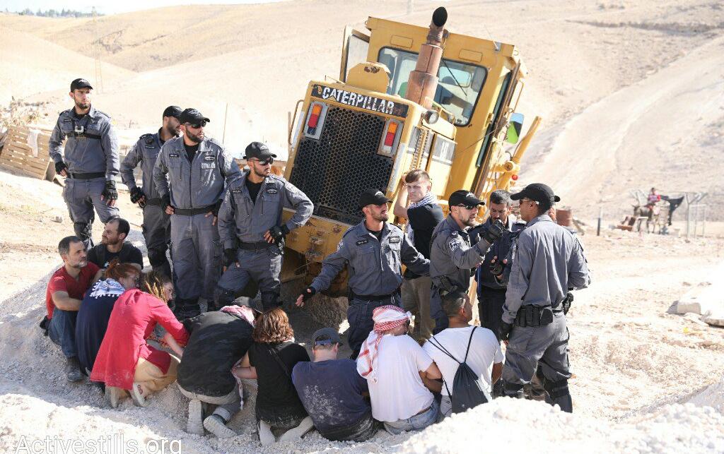 People kneel in front of a Caterpillar bulldozer at Khan al Ahmar village. Credit: ActiveStills.