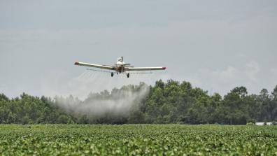 A small low-flying aircraft spraying pesticides on a field of green crops.